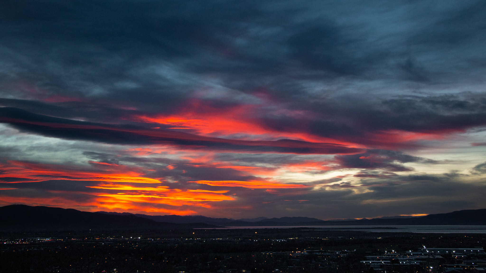 odd horizontal smooth clouds lit orange and pink at sunset over mountains and town